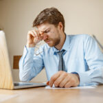 Feeling sick and tired. Frustrated young man massaging his head while sitting at his working place in office