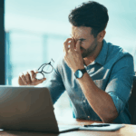 Suplemento para estresse: entenda como o MEDIATE® pode ajudar Homem estressado no trabalho em frente ao computador coçando os olhos - ansiedade e estresse
